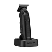 A black BabylissPRO Luminous cordless hair clipper standing upright on its matching black charging base against a plain white background.