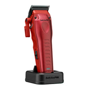 A red BabylissPRO electric hair clipper standing upright on a black charging dock against a plain white background.