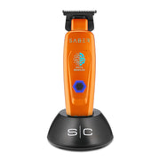 An orange SABER digital brushless electric trimmer standing upright on a black charging base against a white background.